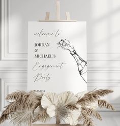 an easel with some flowers on it in front of a sign that says welcome to jordan and michael's engagement party