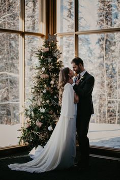 a bride and groom standing next to a christmas tree in front of a large window