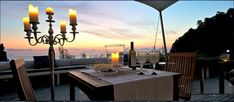 an outdoor dining area overlooking the ocean with candles and wine glasses set on table for two