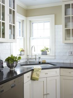 a kitchen with white cabinets and black counter tops is pictured in this image, there are plants on the window sill