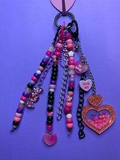 a heart shaped keychain hanging on a purple wall with lots of beads and charms attached to it