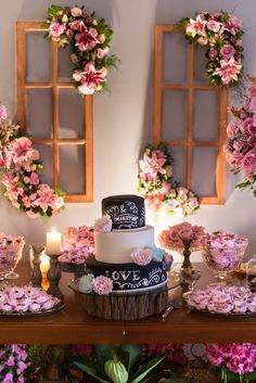 a table topped with a cake covered in pink flowers next to two windows and candles