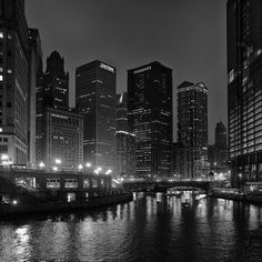 a black and white photo of a city at night with lights reflecting in the water