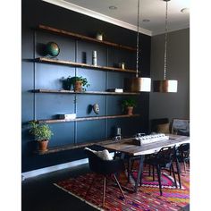 a dining room table with chairs and shelves on the wall behind it, along with potted plants