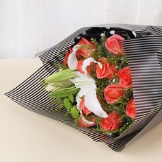 a bouquet of red roses and white orchids wrapped in black paper on a table