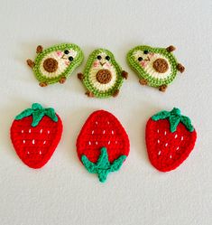 four crocheted strawberries and two small stuffed animals sitting next to each other