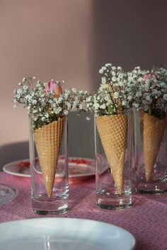 three ice cream cones with flowers in them are on a pink and white tablecloth