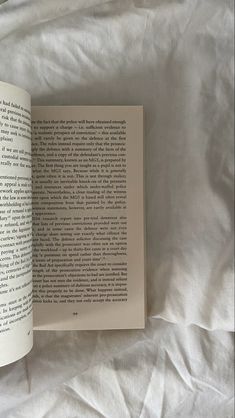 an open book sitting on top of a bed next to a white sheet covered wall