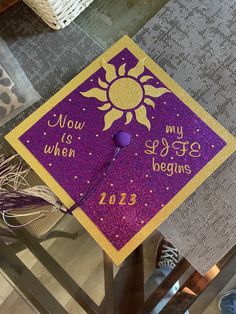 a purple and gold graduation cap with the words now is when my life begins on it