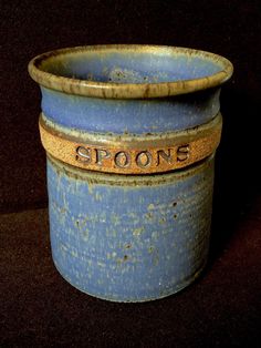 an old blue pot with the word spoons written on it's side sitting on a black surface