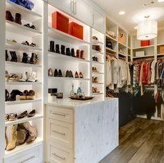 a walk in closet with white shelving and lots of shoes on the counter top