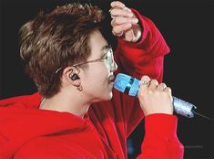 a boy with glasses holding a microphone up to his ear and wearing a red hoodie