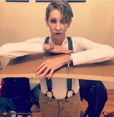 a woman sitting at a table with her hands on top of the table and wearing suspenders