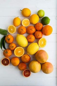 oranges, lemons and limes are arranged on a white surface with leaves