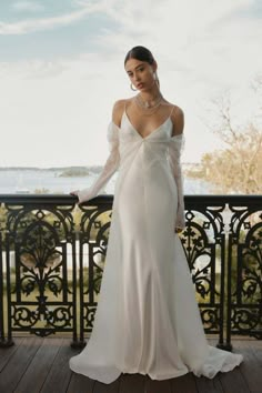 a woman in a white wedding dress standing on a balcony with her hands on her hips