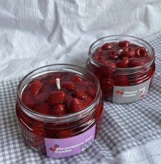 two jars filled with raspberries sitting on top of a checkered table cloth