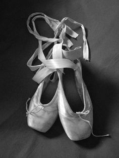 black and white photograph of ballet shoes with ribbons tied around the toes, on a dark background