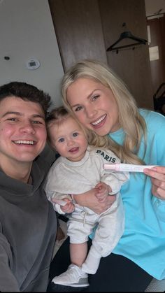 a man and woman holding a baby while they are brushing their teeth with an electric toothbrush