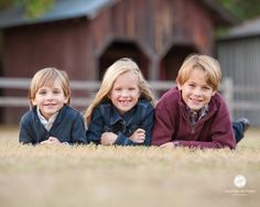 three children laying on the ground in front of a barn