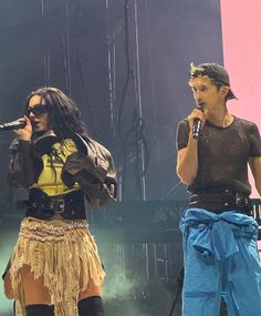 two people standing on stage with microphones in their hands and one person wearing a costume