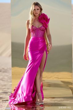 a woman in a long pink dress is walking on the beach with her leg up