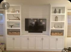 a living room with white bookcases and a flat screen tv mounted on the wall