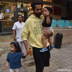 a man walking down the street with two small children on his shoulders and an adult holding onto him