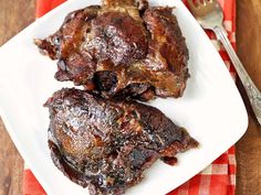 two pieces of meat on a white plate with a fork and knife next to it