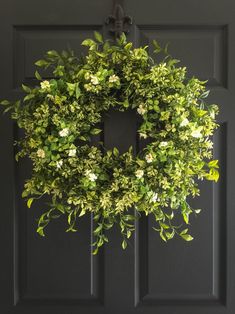 a wreath hanging on the front door with white flowers and greenery around it's edges