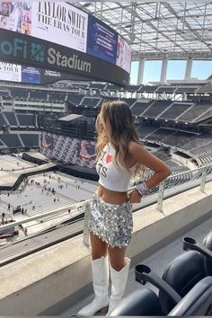 a woman in white boots standing on the sidelines at a stadium with her hands on her hips