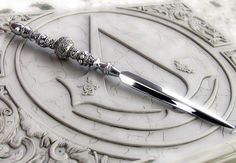 a silver knife sitting on top of a white table next to a circular object with ornate designs