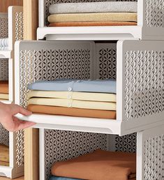 a person is reaching for some folded cloths on a shelving unit in a closet