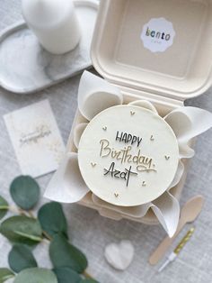 a birthday card in a box on a table with flowers and plates around it,