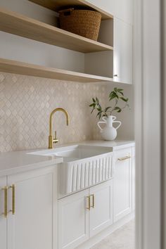 a kitchen with white cabinets and gold faucets on the counter top, along with a vase filled with green plants