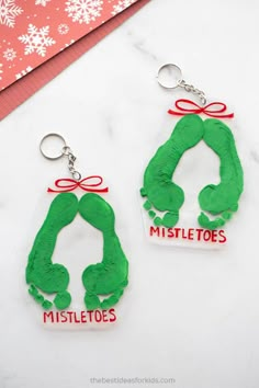 two green handprinted earrings with the word mistle toes on them and a red ribbon