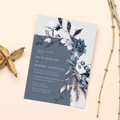 a blue and white floral wedding card on top of a table next to dried flowers