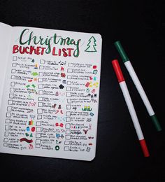 a christmas bucket list with markers and pens on a black surface next to a notebook