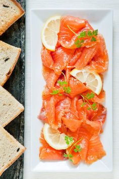 there are slices of bread and salmon on the plate next to each other with lemon wedges