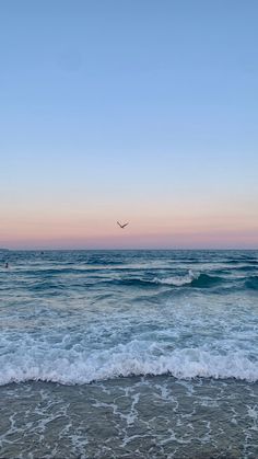 a bird flying over the ocean at sunset