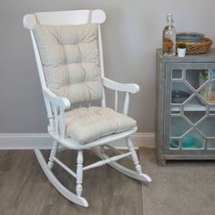 a white rocking chair next to a gray side table with a bottle on top of it