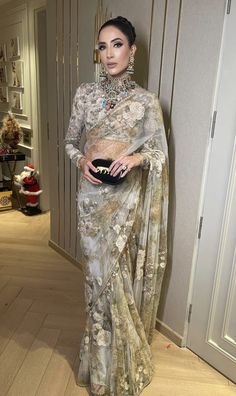 a woman in a white and gold sari standing next to a wall with jewelry on it