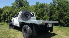 a white truck parked on top of a grass covered field in front of some trees