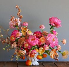 a white vase filled with lots of pink and orange flowers on top of a wooden table