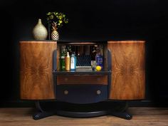 a cabinet with liquor bottles and vases on top of it in front of a black wall