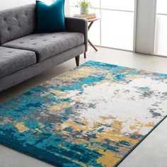 a gray couch sitting next to a blue and yellow rug on top of a floor