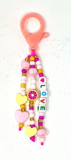 a pink and yellow beaded keychain hanging on a white wall with the word love spelled in small letters