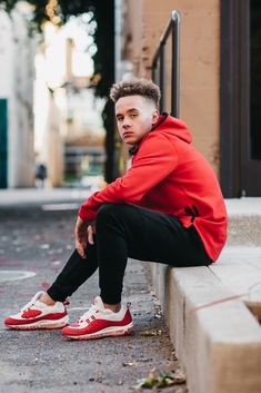 a young man sitting on the curb wearing red sneakers