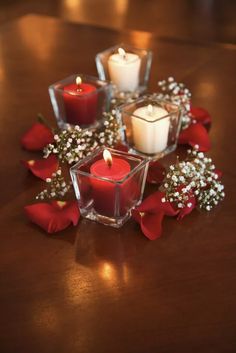 candles and flowers sit on a table with red roses in the center, surrounded by small glass cubes