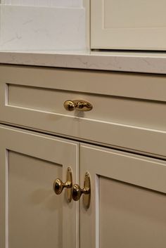 a kitchen with white cabinets and gold pulls on the handles, along with marble counter tops