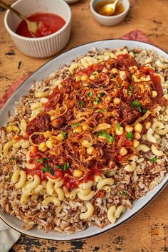 a white plate topped with pasta and meat covered in sauce next to bowls of condiments